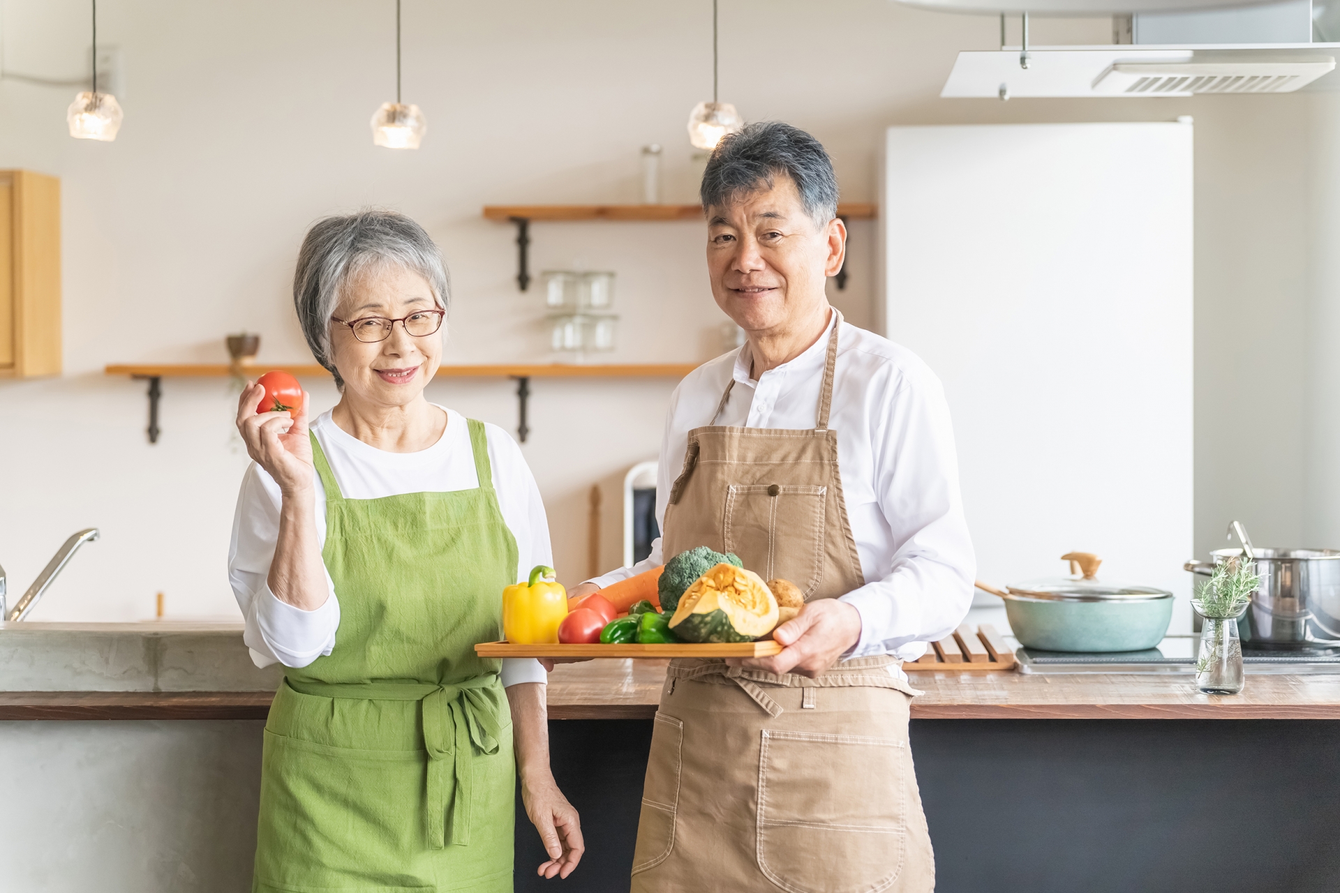 キッチンの前で笑顔で野菜をもつ高齢者夫婦