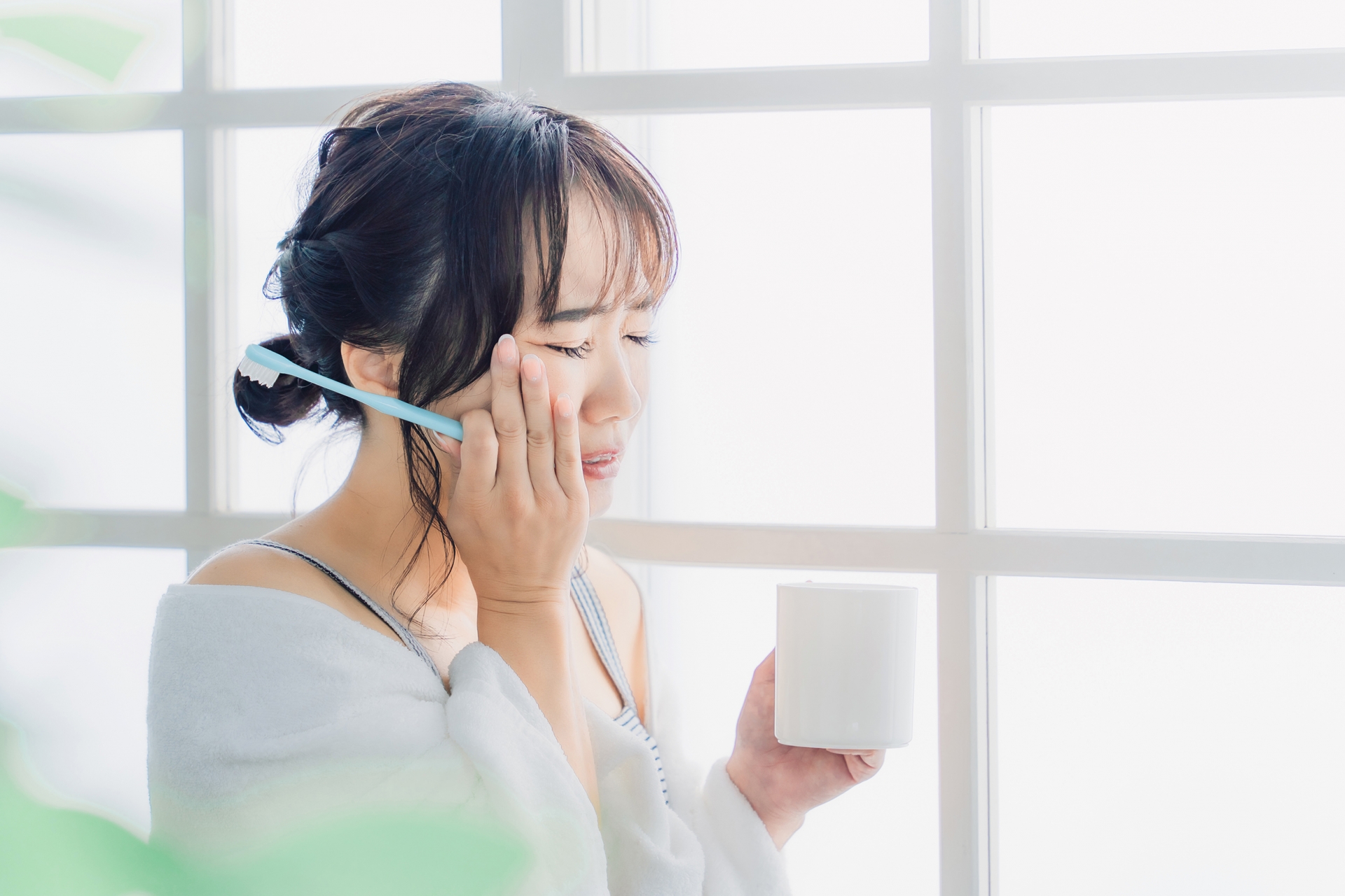 虫歯が痛い・しみて頬を押さえる女性の横顔
