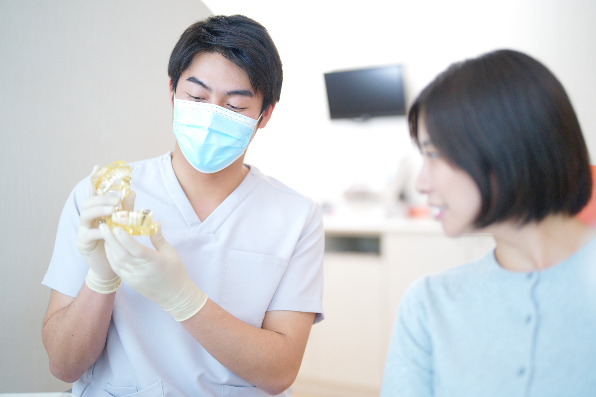 歯の模型を見せる歯科医と見つめる患者の横顔