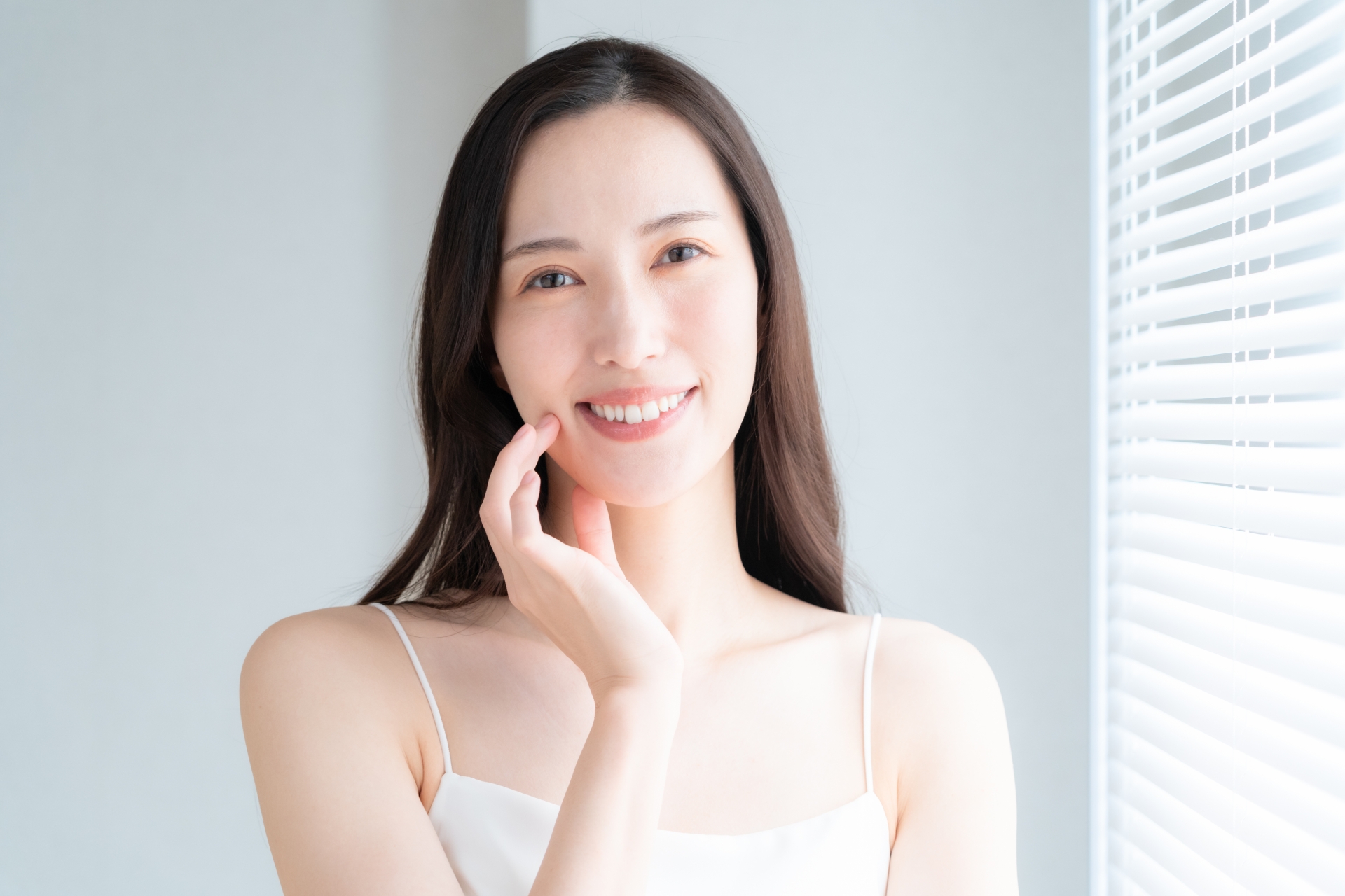 窓際でスキンケアをする若い女性